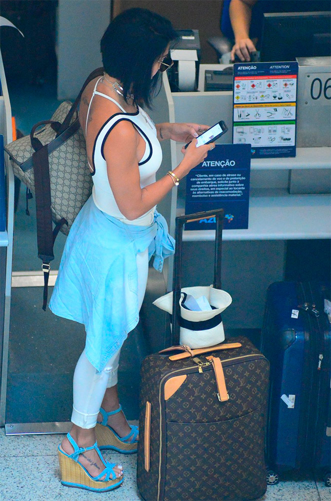 Bella Falconi não desgruda do celular durante check-in em aeroporto