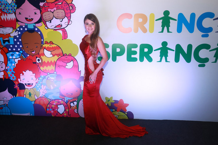 Para tudo! Paula Fernades usa vestido vermelho com fenda lateral e mostra cinturinha na gravação do Criança Esperança