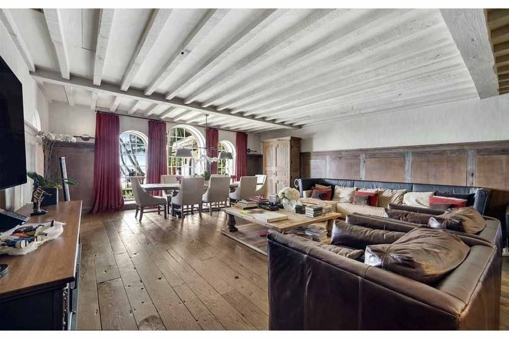 Nesta área de estar encontramos janelas deslumbrantes, uma mesa de madeira e cadeiras ao lado de um sofá enorme e televisão