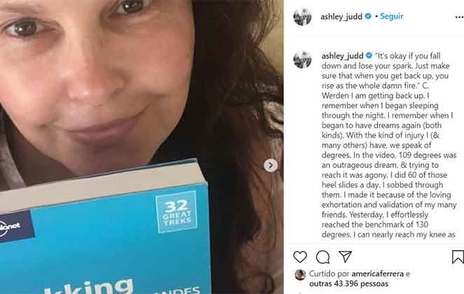Ashley Judd deitada na cama, lendo um livro