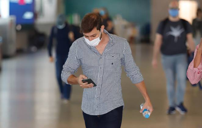 Caio mexendo no celular em aeroporto