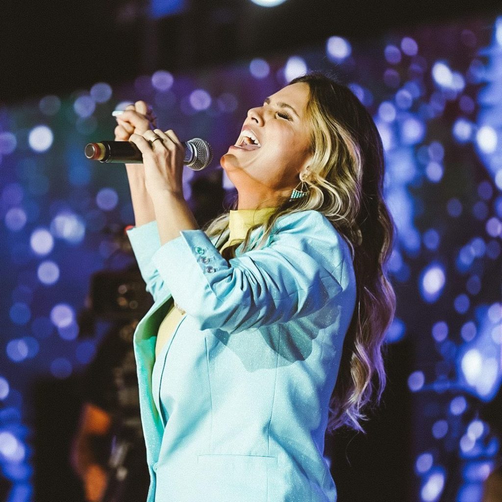 Aline Barros no palco, cantando de roupa azul