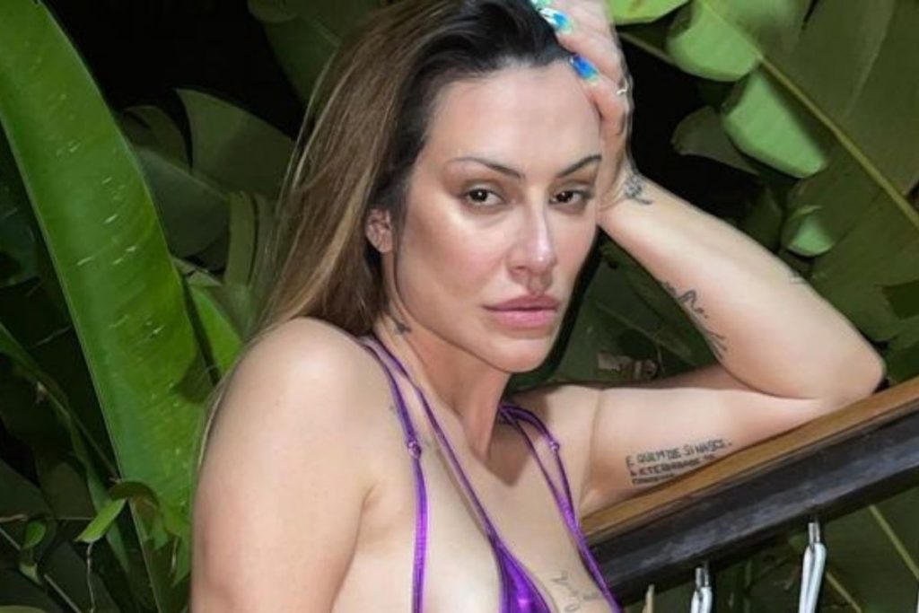 Cleo com top roxo e mostrando tatuagem