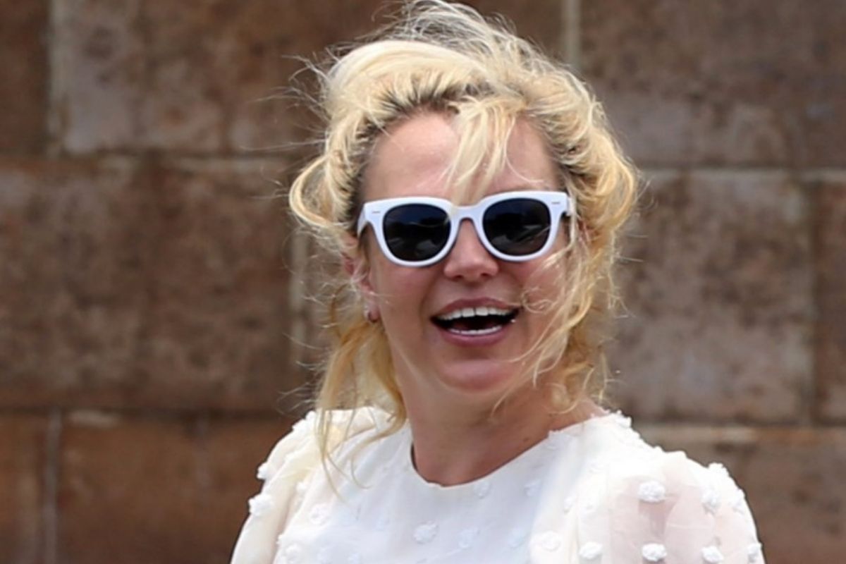 Britney Spears, sorrindo, de blusa branca e óculos escuros
