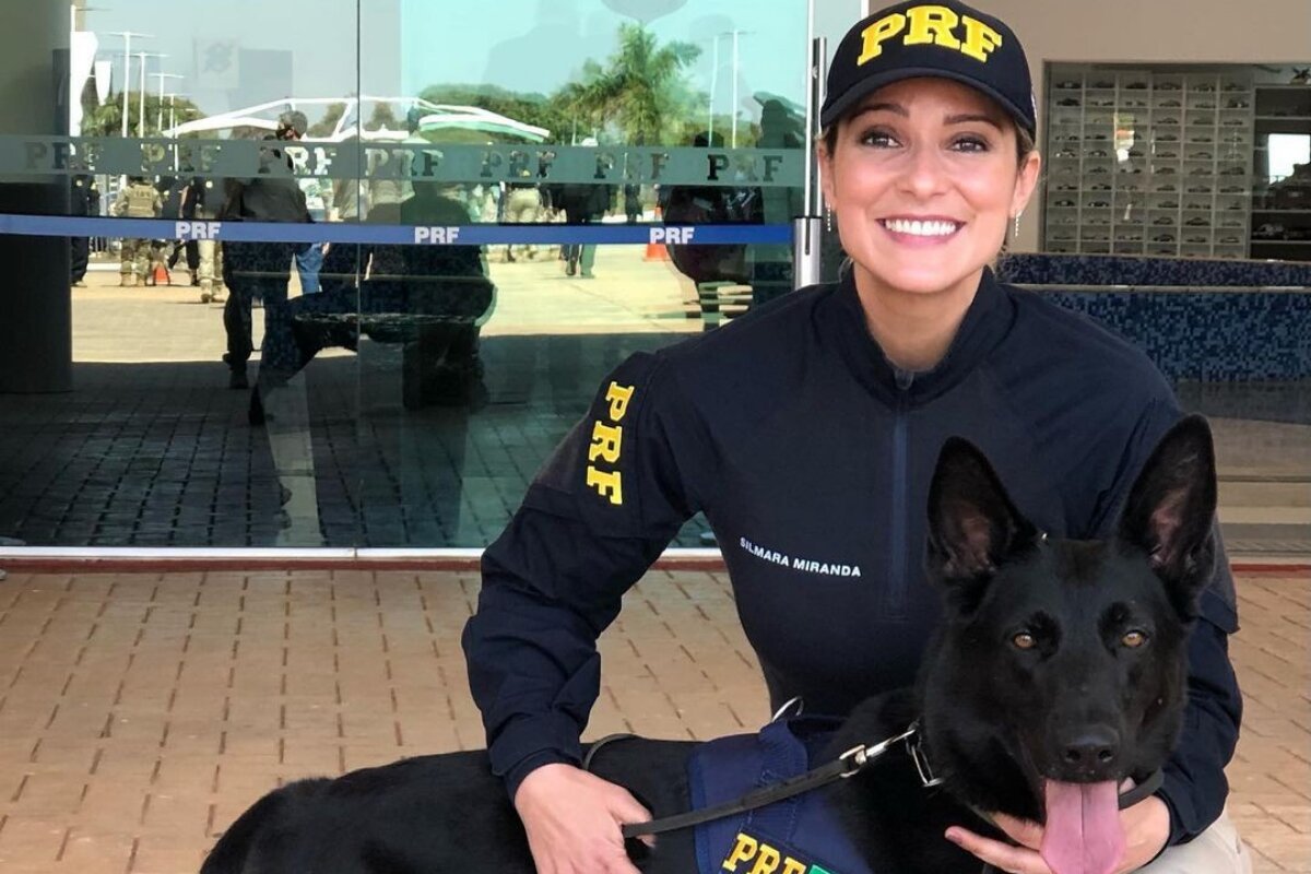 Silmara Miranda com uniforme da Polícia Rodoviária Federal, segurando um cachorro preto