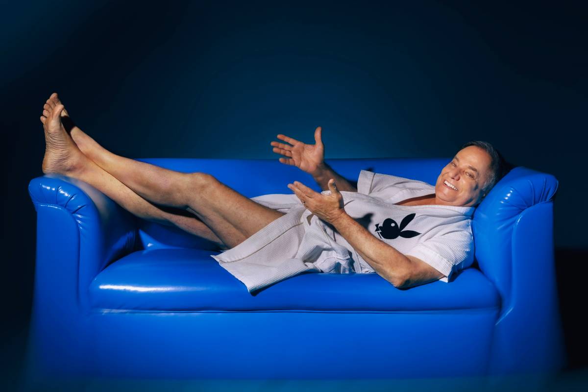 ronnie von posando deitado com roupão da playboy em sofá de cor azul