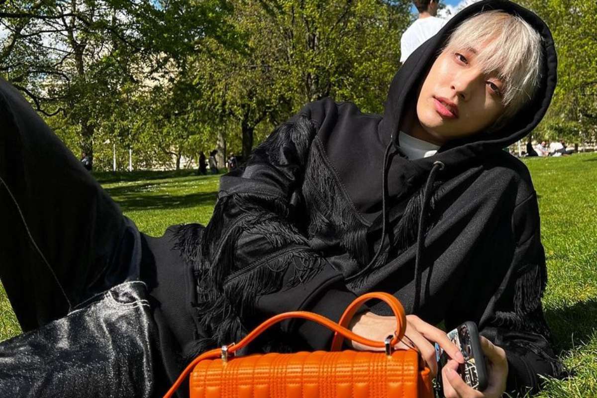 cantor de k-pop holland deitado de casaco preto na grama