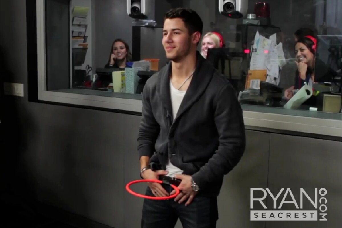 Nick Jonas, de preto, com uma cesta de softball na cintura