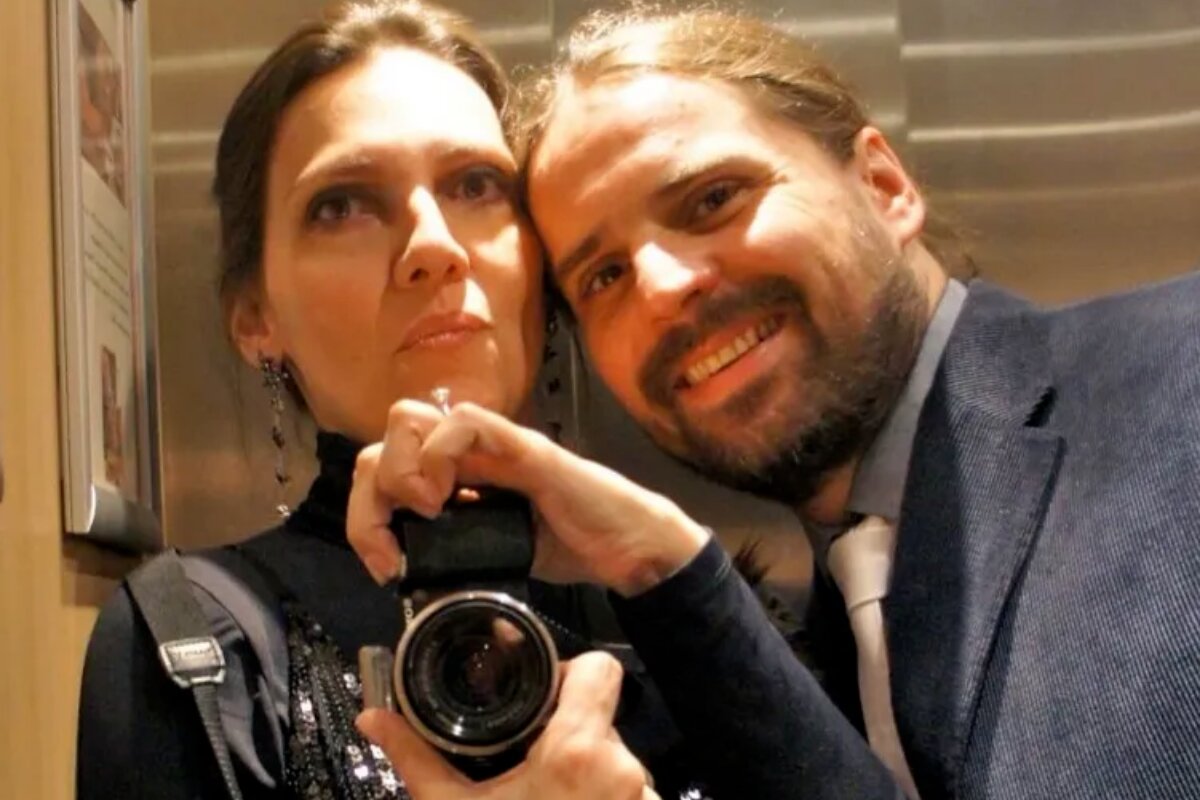 Patrícia Kisser segurando umacâmera, abraçada ao marido, Andreas Kisser, ambos sorrindo, fazendo selfie