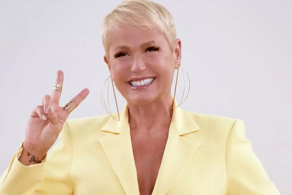 Xuxa de amarelo, fazendo sinal de positivo, sorrindo