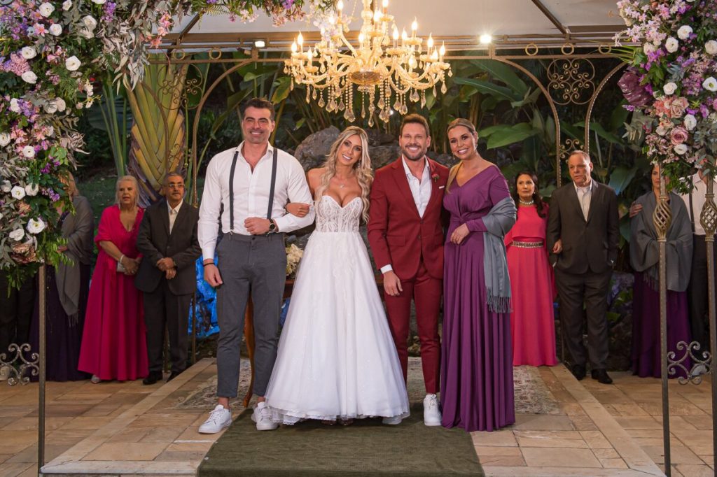 JP Mantovani de camisa branca, suspensório e calça cinza, os noivos e  Renata Banhara de vestido roxo 