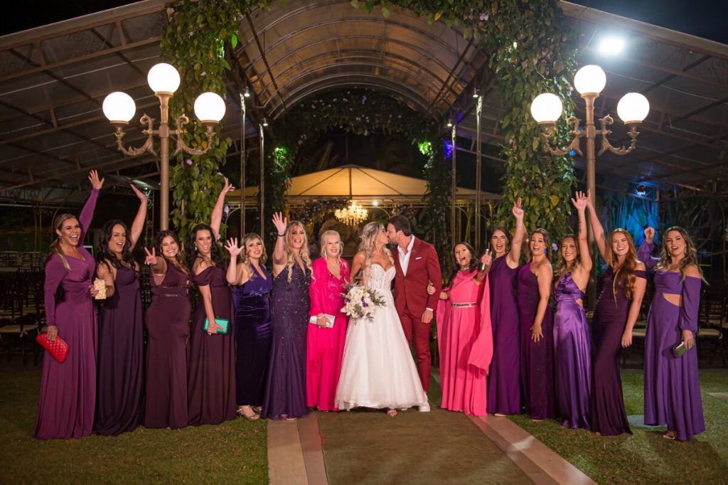 Madrinhas de vestido, roxo (a maioria) e rosa, ladeando os noivos