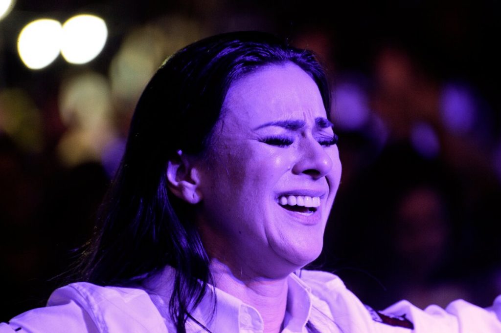 Mulher chorando, de camisa branca e olhos fechados