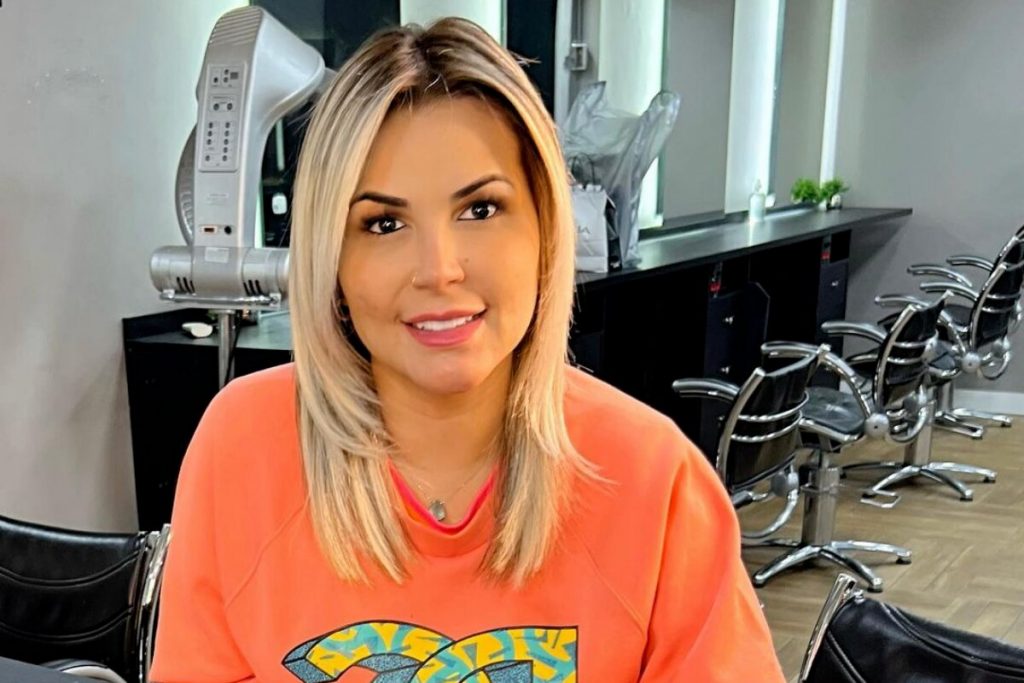 Deolane Bezerra sem o mega hair, de moletom laranja, sentada, sorrindo