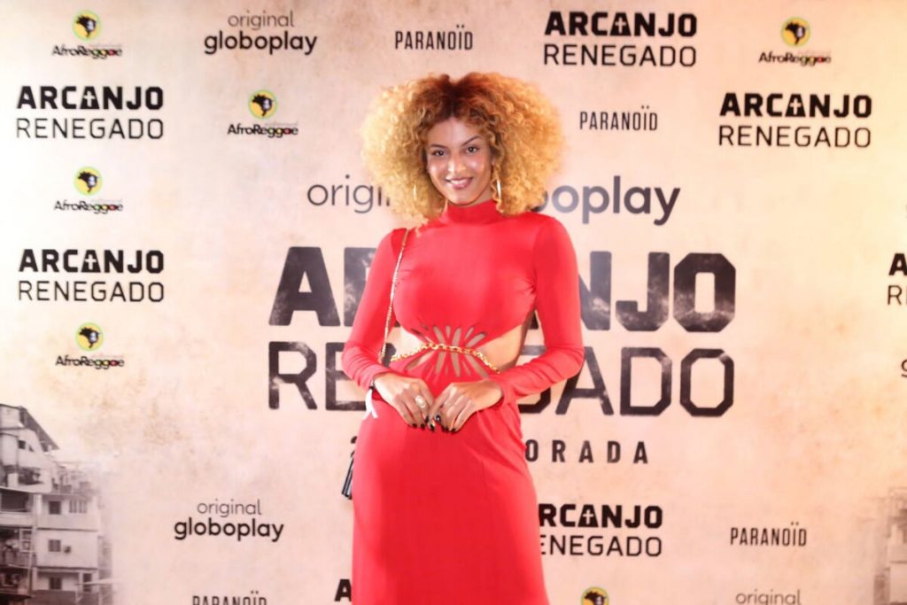 Gabriela Loran de vestido vermelho, posando no backdrop de Arcanjo Renegado