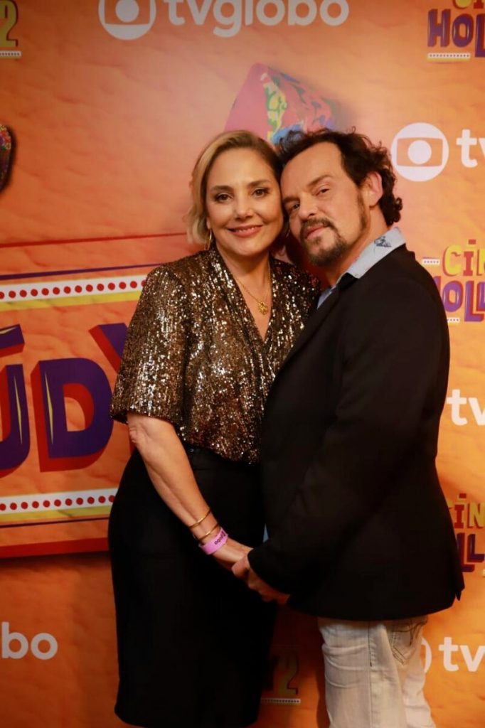 Heliosa Perissé de blusa doirada e saia preta, e Matheus Nachtergaele de preto. abraçados