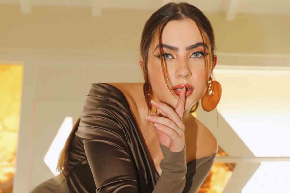 Jade Picon com o dedo na boca, sensualizando, de blusa de manga marrom