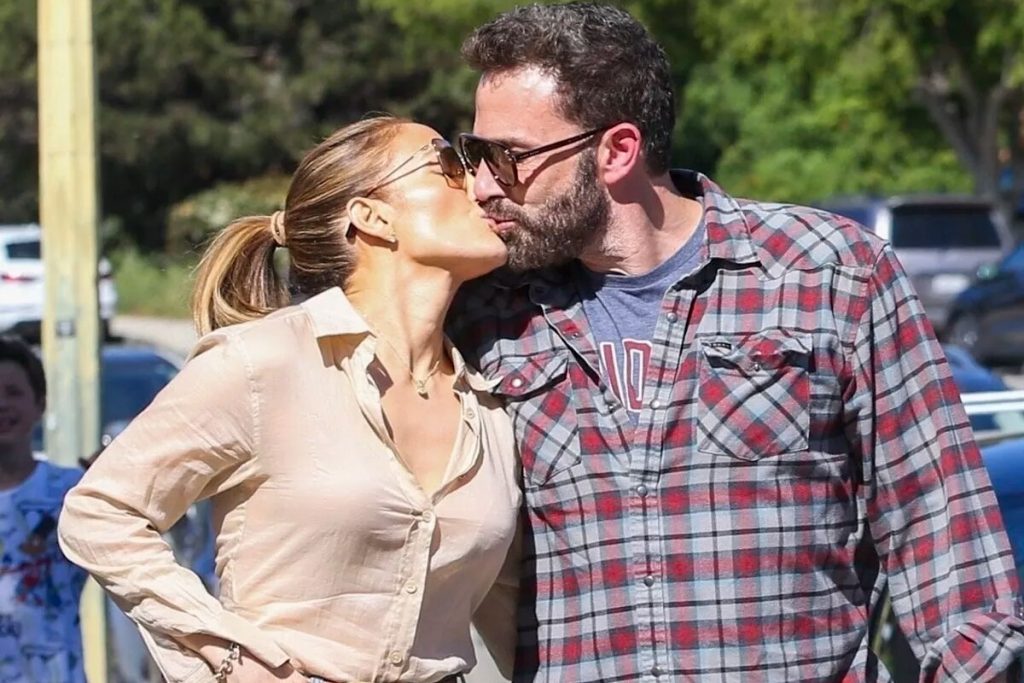 Jennifer Lopez de camisa de manga bege e e Ben Affleck, de camisa xadrez, na rua, se beijando