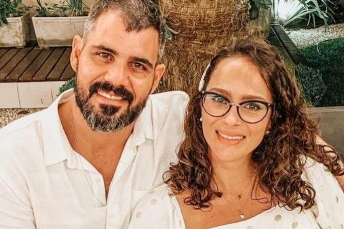 Juliano Cazarré e a mulher, Letícia, de óculos, ambos de branco, sorrindo