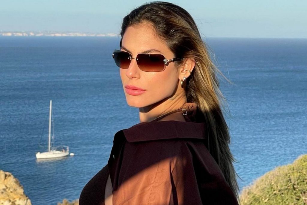 Mari Gonzalez de óculos escuros e echarpe preta, com uma praia de fundo 