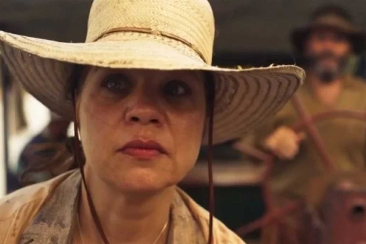 Maria Bruaca (Isabel Teixeira) de chapéu, na chalana, em cena de Pantanal