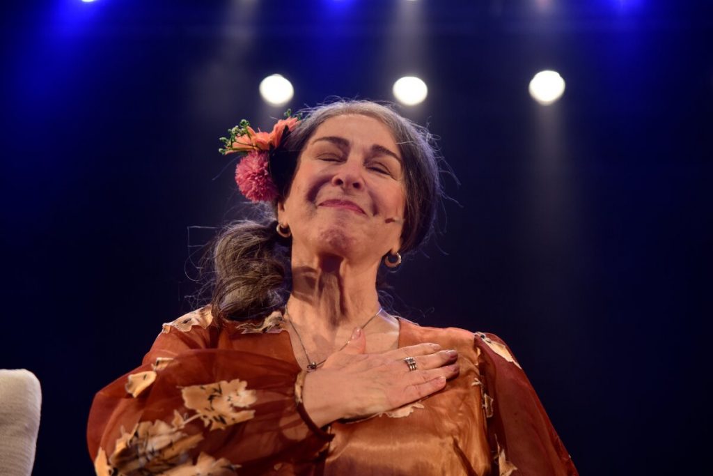 Nívea Maria  o palco, com a mão no peito, caracterizada, com uma flor no cabelo