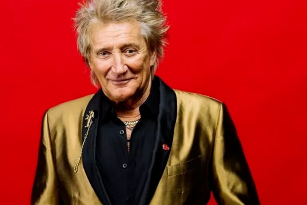 Rod Stewart de terno dourado, fundo vermelho