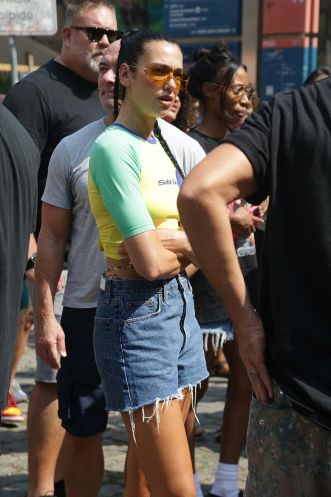 Dua Lipa com camisa verde e amarela, bermuda jeans, cercada por seguranças, andando na Feira do Lavradio, na Lapa, RJ