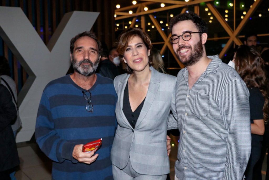 Eduardo Duvivier de camisa listrada azul e grafite, ao lado de Maria Clara Gueiros, de terninho cinza e Bruno Jablonski, de camisa cinza