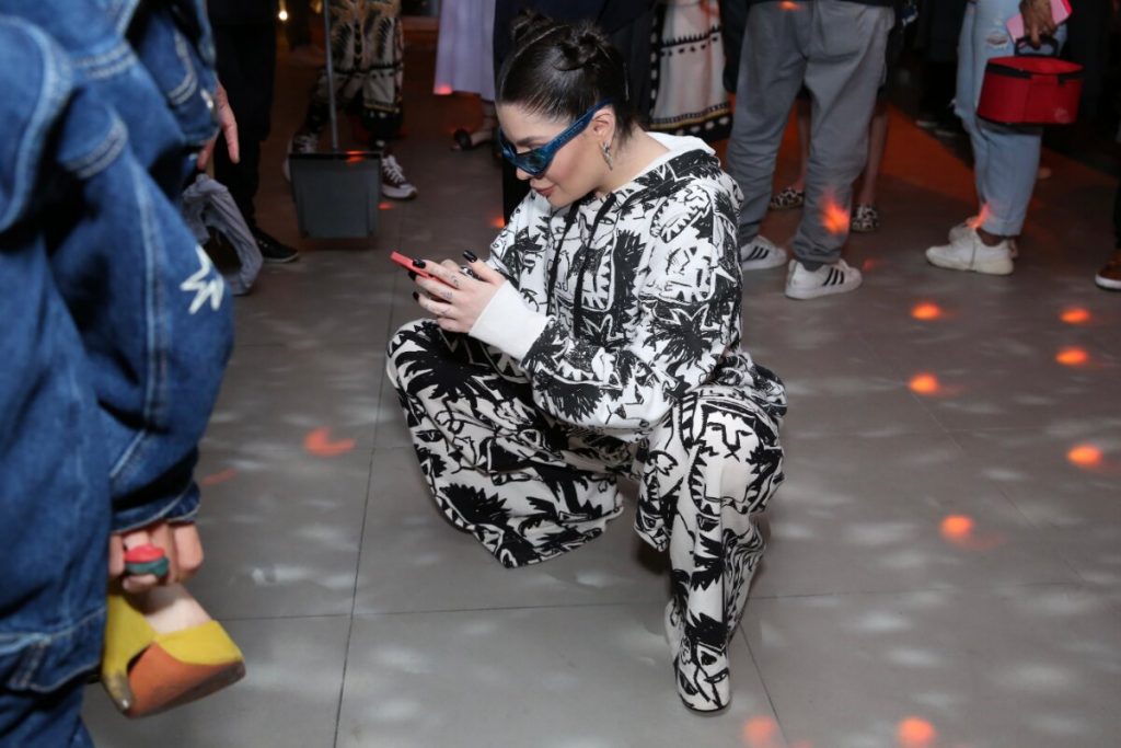 GKay agachada no chão mexendo no celular, de macacão estampado