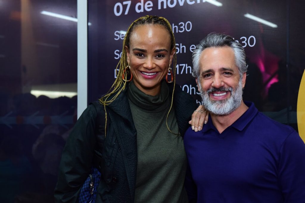 Luciana Melo de verde e preto, com tranças no cabelo, abraçada ao marido, de azul