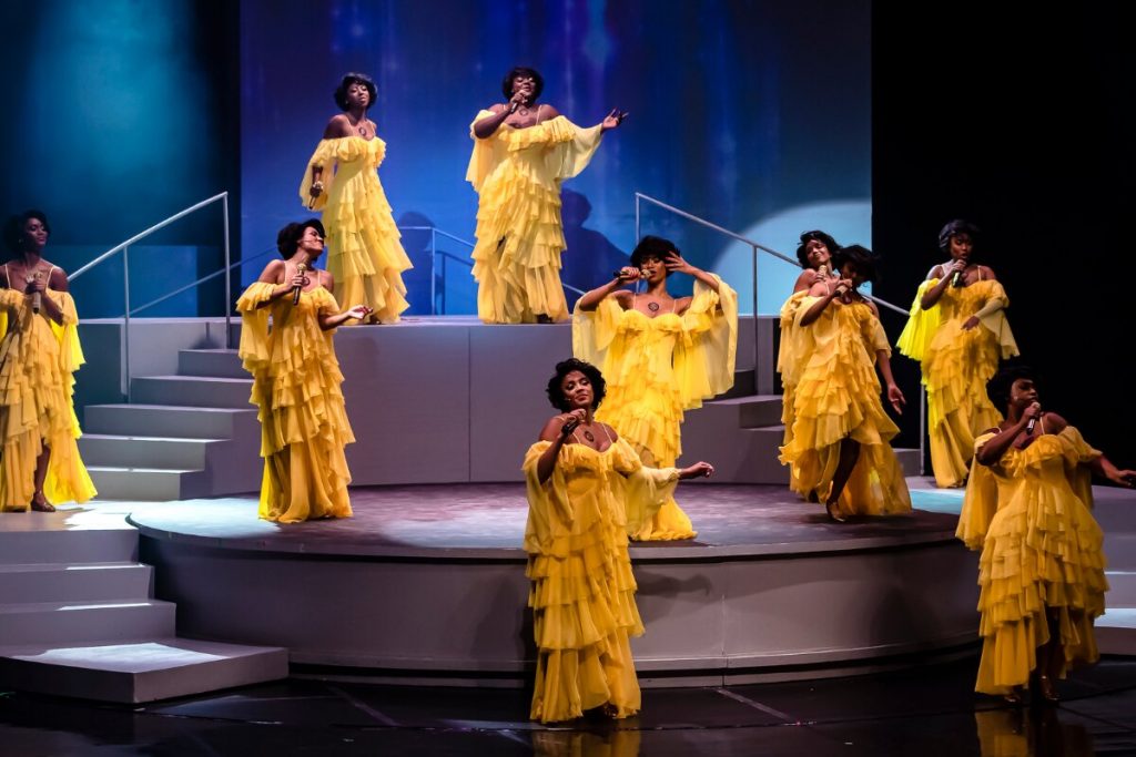 Doze atrizes de vestido amarelo, caracterizadas como Alcione, cantando