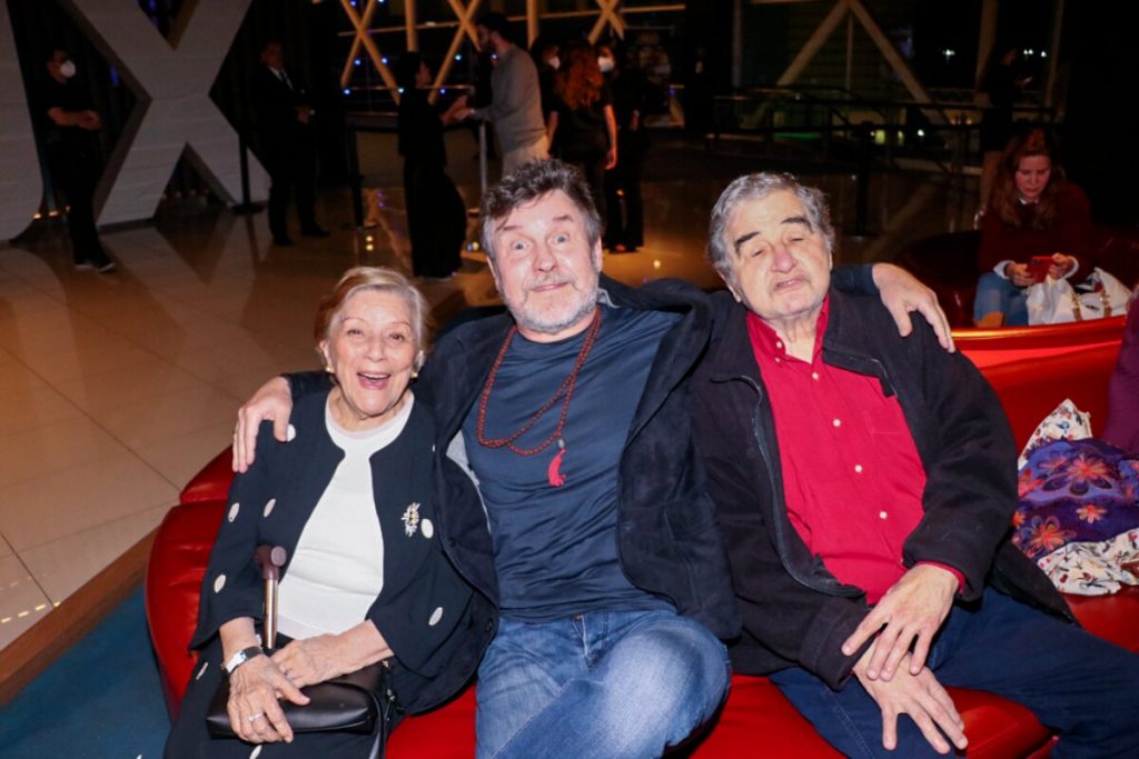 Selma Lopes de camisa branca e casaco preto, sentada ao lado de Antonio Calloni, de azul escuro e jeans, e Otávio Augusto de camisa vermelha, casaco preto e calça jeans