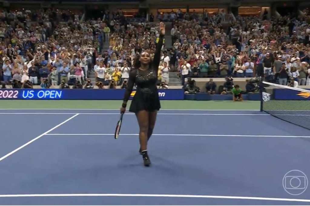 Serena Williams acena para a plateia, com roupa desenhada por ela, cheia de cristais