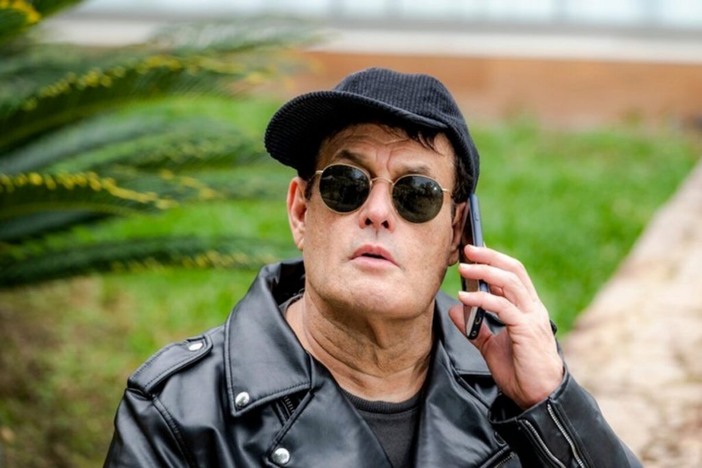 Sergio Mallandro de boné preto, jaqueta preta, camisa preta, falando ao celular, de óculos escuros