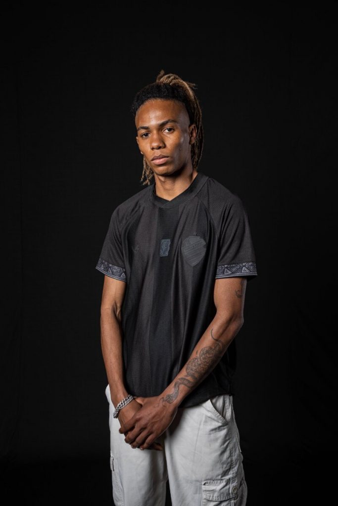 Modelo negro com camisa preta temática da Consciência negra, em pé, de bermuda bege