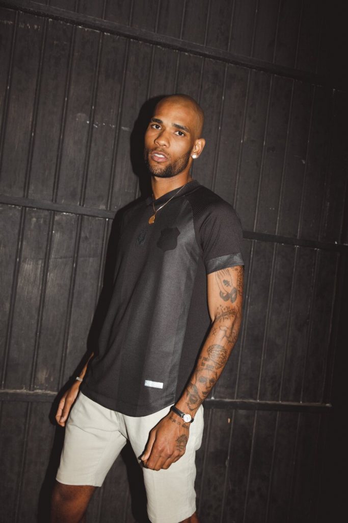 Modelo negro com camisa preta temática da Consciência negra, em pé, de bermuda bege