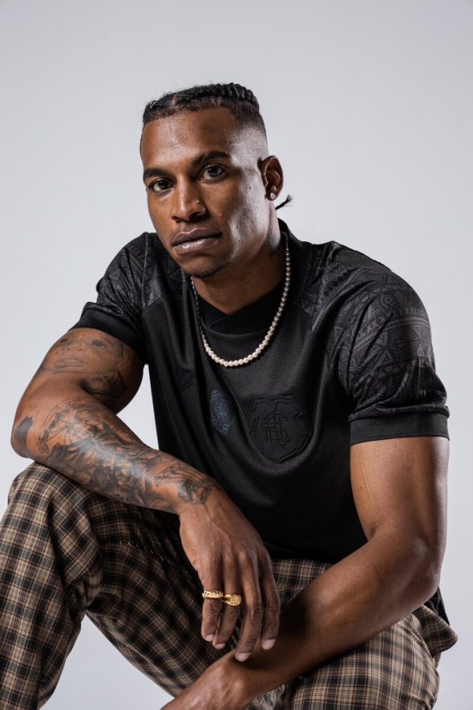 Modelo negro com camisa preta temática da Consciência negra, agachado de calça xadrez marrom e preta