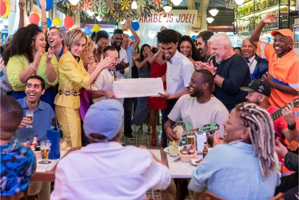 A chegada do bolo de Joel (Nando Cunha) em cena de Travessia