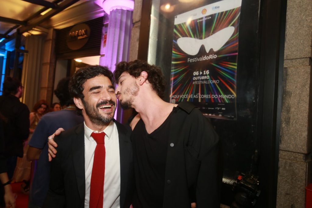 Johnny Massaro, de preto beijando o rosto de Caio Blat, de terno preto