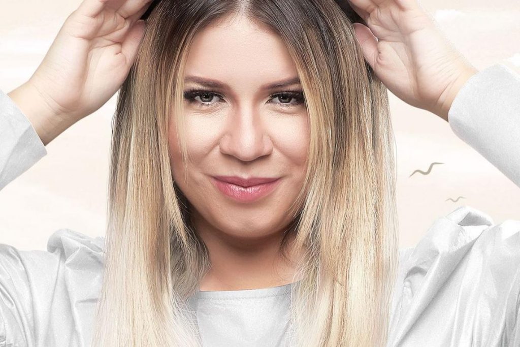 marilia mendonça posando séria em cartaz com look branco