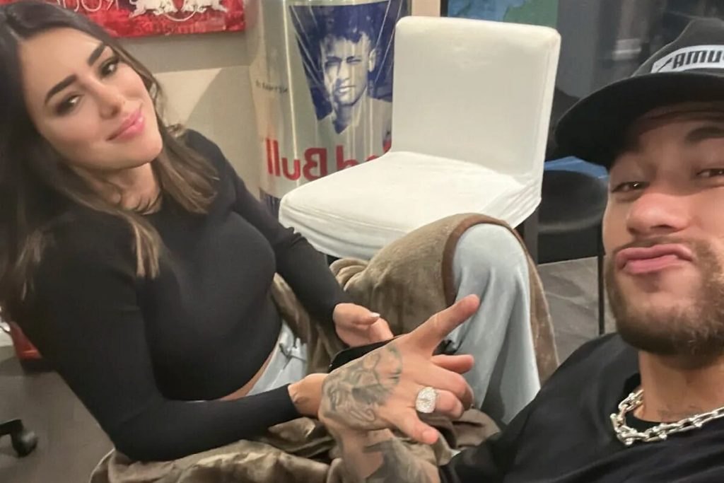 Bruna Biancardi de blusa preta de manga comprida, sentada ao lado de Neymar 