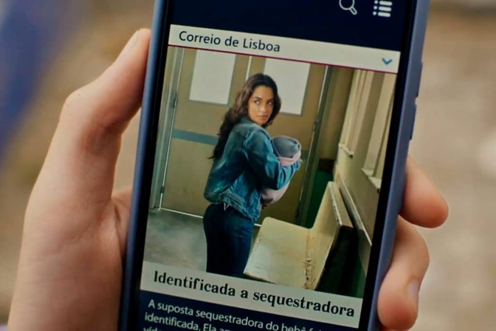 Tela de telefone celular com imagem montada de Brisa (Lucy Alves) segurando um bebê, como reportagem de um jornal português