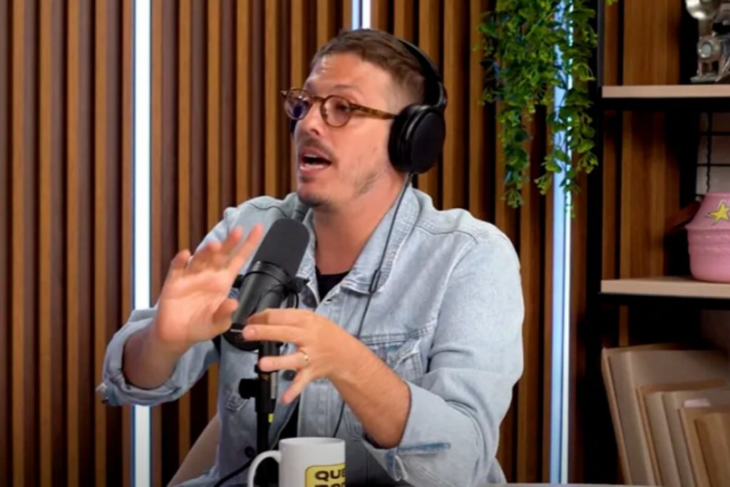 Fábio Porchat diante de um microfone, em estúdio de podcast, de camisa jeans, gesticulando