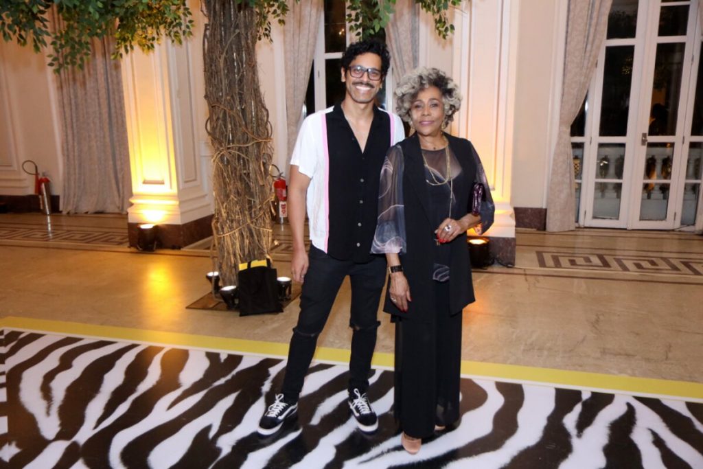 Renan Monteiro e Duh Moraes, abraçados, ambos de preto, ele com camisa branca sobrepostade