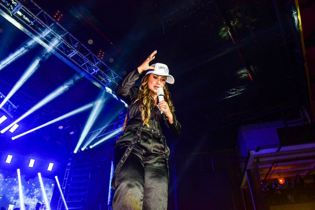 Simone Mendes no palco, de boné branco, calça e camisa preta 