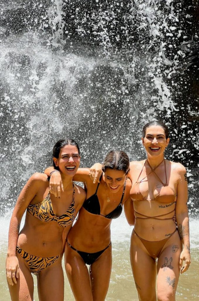 Antonia, Ana e Cleo, todas de biquíni, sorrindo na cachoeira
