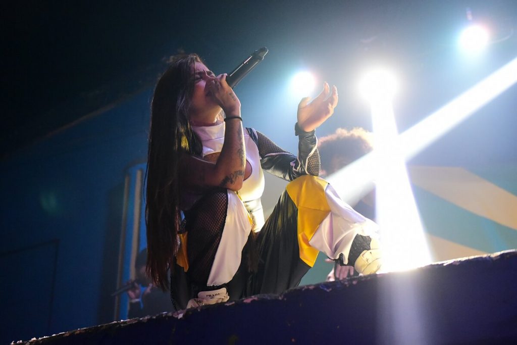 MC Mirella agachada no palco, cantando