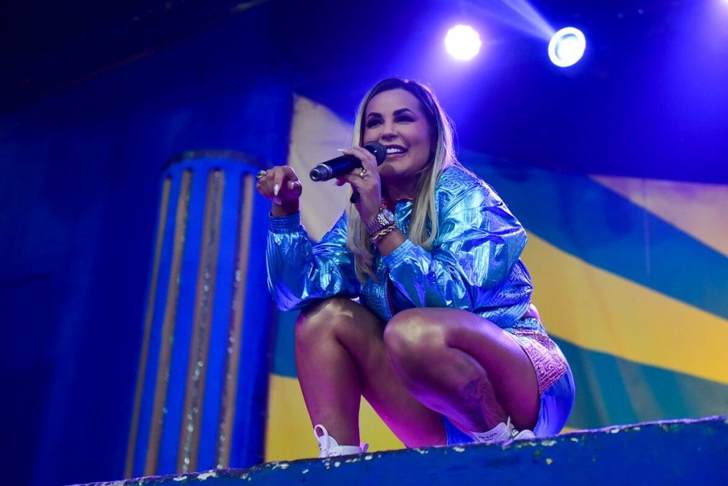 Deolane agachada no palco, falando ao microfone