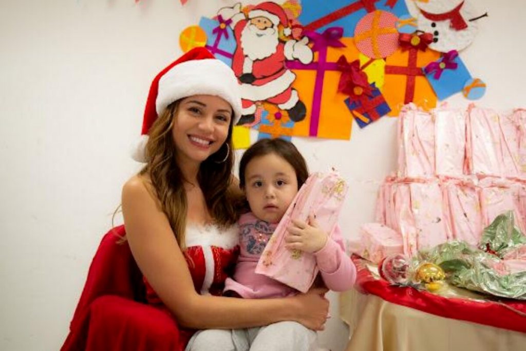 Maria Melilo vestida de Mamãe Noel, sentada com uma criança no colo